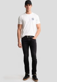 Hvid kortærmet T-shirt med blå grafik på brystet, parret med sorte slim-fit jeans og sorte sneakers med gummisåler.