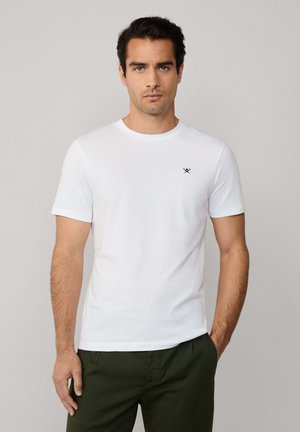 Witte katoenen t-shirt met korte mouwen en een ronde halslijn, met een klein zwart logo op de linkerkant van de borst. Gepaarde met groene broek.