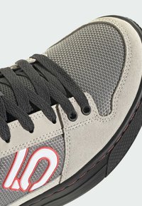 Gray and black sneaker with mesh and suede materials. Features black laces, a padded collar, red accents, and a rubber sole with textured grip.