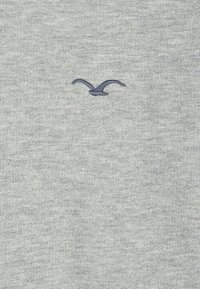 Hellgrauer Pullover aus weicher Stoff, der ein blaues, gesticktes Möwenlogo in der Mitte zeigt. Glatte Textur mit einem klassischen Rundhalsausschnitt.