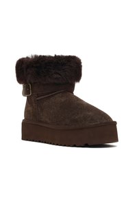 Braune Wildleder-Stiefelette mit breitem Kunstfellbund, verstellbarem Schnallen-Detail und einer strukturierten Plattformsohle für zusätzlichen Grip.