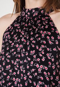 Černý halter top s květinovým vzorem v červené a bílé barvě, s plisovanými detaily a hladkým textilním povrchem.