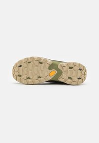 Črna in zelena športna čevljasta podlaga z grobim vzorcem, ki ima teksturirano gumijasto površino in izrazit rumen logotip Vibram.