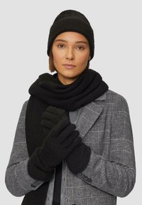 Schwarze gestrickte Mütze, Schal und Handschuhe aus weicher Textur, die über einem grauen karierten Mantel getragen werden. Die Accessoires sind in Farbe und Design einheitlich und bieten Wärme.