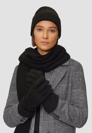 Zwarte gebreide muts, sjaal en handschoenen in zachte textuur gedragen over een grijs geruit jasje. De accessoires zijn uniform in kleur en ontwerp en bieden warmte.