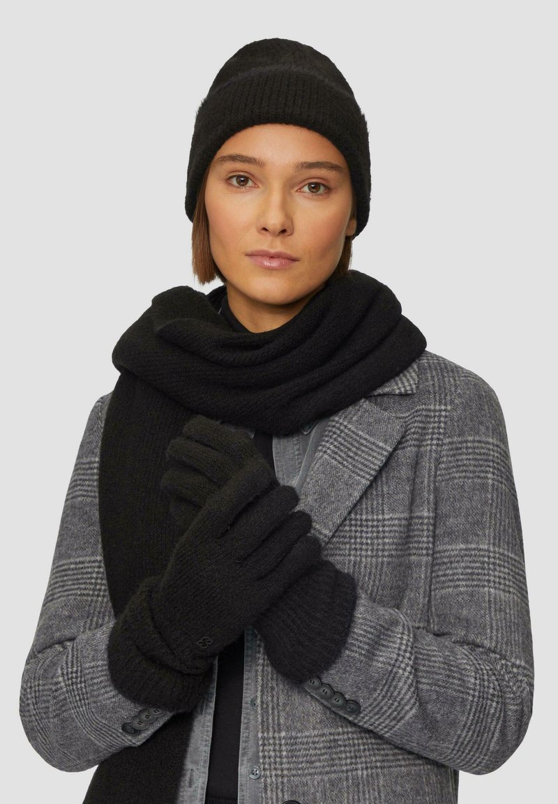Schwarze gestrickte Mütze, Schal und Handschuhe aus weicher Textur, die über einem grauen karierten Mantel getragen werden. Die Accessoires sind in Farbe und Design einheitlich und bieten Wärme.