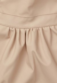 Ljust beige tyg med en slät yta och subtil lyster, som har samlade detaljer och kontrasterande sömmar nära toppen.