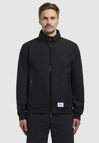 Chaqueta negra con cremallera, cuello alto, bolsillos laterales y puños acanalados. Confeccionada en tejido suave con una etiqueta de logo en el dobladillo.