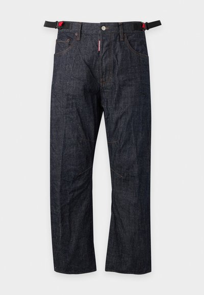 Jean en denim bleu foncé avec des sangles latérales noires réglables et un bouton supérieur visible sur un fond uni.