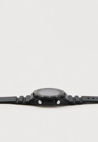 Czarny cyfrowy zegarek z pomarańczowymi akcentami, okrągłą tarczą, teksturowanym pierścieniem i elastycznym gumowym paskiem z rowkowanym wzorem.