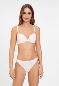 Lichtroze kanten beha met voorgemoldde cups en verstelbare banden, gecombineerd met bijpassende transparante slipjes met een klein strikje op de taille.