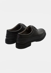 Black leather shoes with a rounded toe, lace-up design, and pronounced textured rubber soles featuring horizontal ridges.