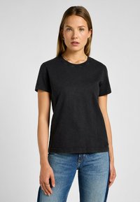 T-shirt nera in cotone a maniche corte, con scollatura a girocollo e una vestibilità leggermente ampia, abbinata a jeans azzurri chiari con spacchi laterali.