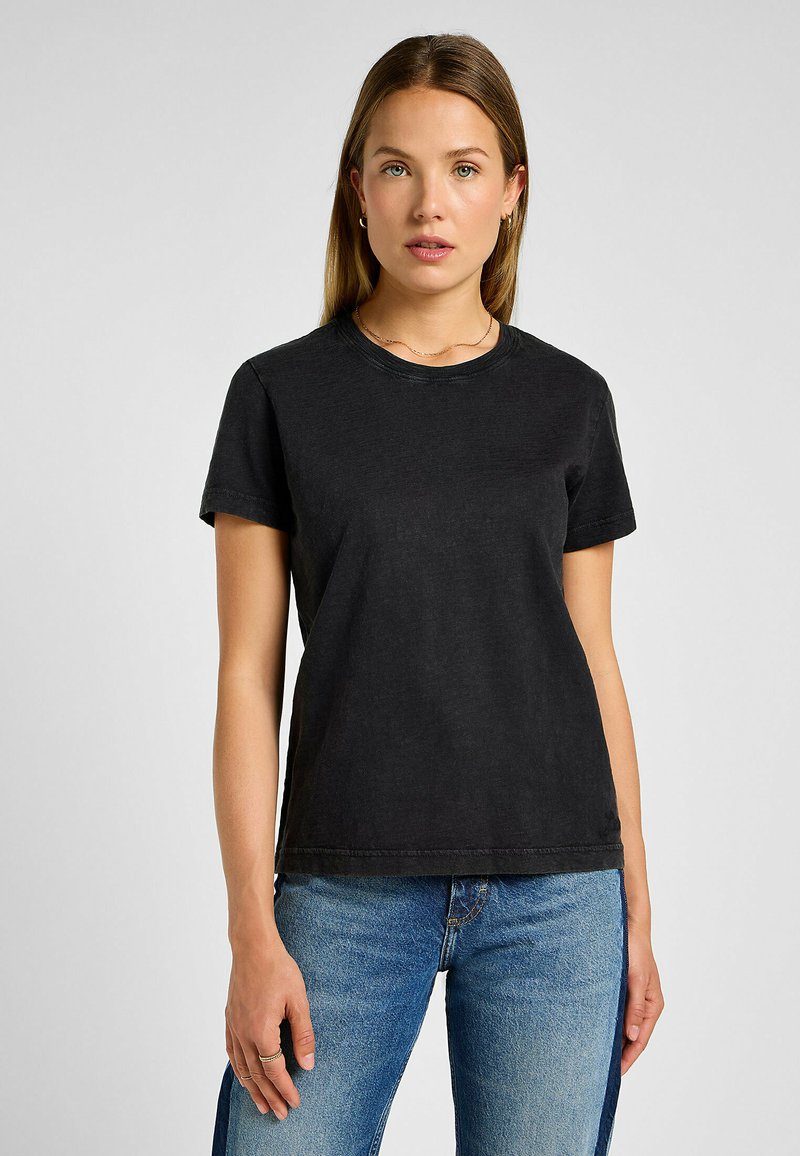 T-shirt nera in cotone a maniche corte, con scollatura a girocollo e una vestibilità leggermente ampia, abbinata a jeans azzurri chiari con spacchi laterali.