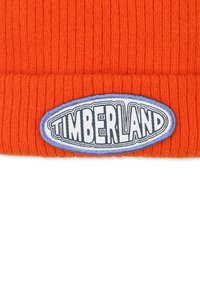 Oranje geribde gebreide beanie met een blauwe ovale badge waarop "TIMBERLAND" in witte letters in het midden is geborduurd. Zachte textuur.