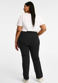 Mustat suorat lahkeet -farkut, joissa on takataskut, yhdistettynä valkoiseen lyhythihaiseen t-paitaan. Sileä kangas ja vähäiset ompeluyksityiskohdat.