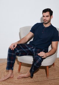 Set de pijama bleumarin format dintr-un top cu mânecă scurtă și pantaloni cu carouri. Topul are un placket cu nasturi și un guler în carouri. Pantalonii au un model în nuanțe de albastru, roșu și alb.