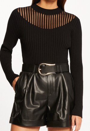 Mujer vistiendo un suéter negro acanalado con canesú de rayas transparentes, combinado con pantalones cortos de cuero sintético negro de talle alto y cinturón con hebilla plateada.