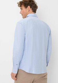 Hellblaues, langärmliges Hemd mit Kragen, das eine glatte Textur und einen dezenten Glanz aufweist. Mit Knopfakzenten an den Ärmeln.
