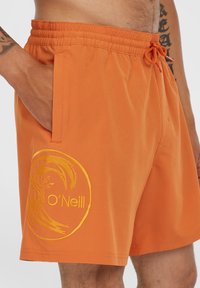 Bañadores naranja hechos de tejido ligero, con una cintura elástica, bolsillos laterales y un logo de O'Neill bordado en amarillo.