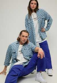 Camicie a quadri blu chiaro sopra t-shirt bianche, con pantaloni blu e sneakers bianche. Caratteristiche includono tasche e schemi di colore a contrasto.