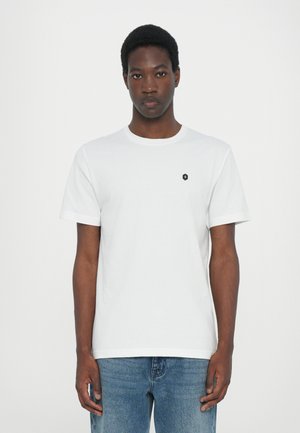 T-shirt en coton blanc avec un col ras du cou, des manches courtes et un petit logo noir sur la poitrine gauche. Texture lisse, coupe décontractée.