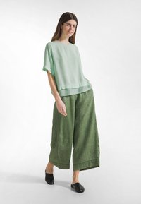 Jasnozielony top z krótkim rękawem z warstwowym dołem; zestawiony z luźnymi, fakturowanymi ciemnozielonymi spodniami i czarnymi butami wsuwanymi.