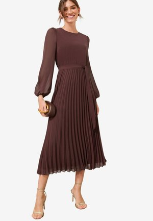 Braunes, plissiertes Midikleid mit langen Ärmeln, Rundhalsausschnitt und einem Gürtel in der Taille. Kombiniert mit goldenen, schmalen High Heels und einer Clutch.