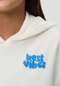 Weißer Hoodie mit weichem, plüschigem Material und einem blauen, in Bubble-Print gestalteten „best vibes“-Grafik auf der Vorderseite. Gemütliches und lässiges Design.