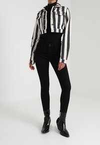 Korta jeansjacka med horisontella svartvita ränder, bärs över en figurnära svart tröja och svarta tighta byxor, kombinerat med glansiga svarta stövlar.