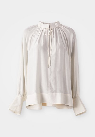 Blusa di seta bianca con colletto alto, scollatura arricciata e maniche lunghe con polsini svasati e una leggera lucentezza.