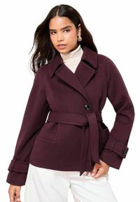 Vyno raudonos spalvos paltas su diržu juosmens srityje, apykakle, sagų užsegimu ir šoninėmis kišenėmis. Pagamintas iš tekstūruotos medžiagos, turi platūs rankoves ir rankogalius.