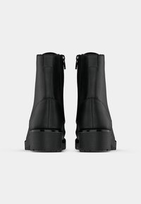 Bottines noires à cheville avec une finition en cuir lisse, bout carré, zips latéraux et semelles en caoutchouc épaisses. Design minimaliste sans matériel visible.