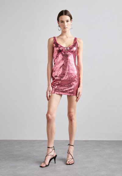 Vestido mini de lentejuelas rosas con escote en forma de barco, que presenta un ribete en contraste y una hebilla decorativa central. Combinado con tacones negros con tiras.