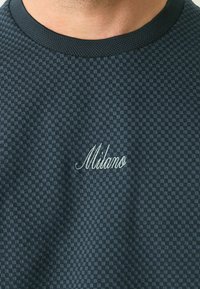 Tamno karirani kratkotrajni rukav polo majica s okruglim izrezom i izvezenim detaljem "Milano" na donjem desnom dijelu u svijetloj konci.