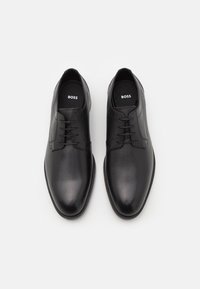 Chaussures en cuir noir à finition lisse, bout arrondi et lacets. La semelle intérieure est ornée de la marque "BOSS" imprimée en blanc.