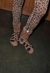 Leopardenmuster-Leggings in Braun und Schwarz kombiniert mit flauschigen braunen Socken, die ein ähnliches Muster aufweisen. Die Socken haben ein lässiges Design.