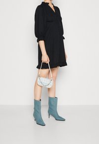 Abito nero con maniche a sbuffo, abbottonato davanti e con orlo arricciato, abbinato a stivaletti in denim azzurro a caviglia e a una piccola borsa a tracolla blu a fantasia.