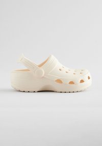 Világosbarna papucsok könnyű műanyagból, szellőzőlyukakkal, hátsó pánttal és texturált talpakkal a jobb tapadás érdekében. Simított felületű kivitel.