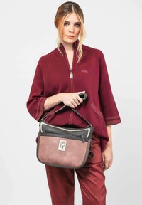 Bolso de hombro marrón y rosa con textura de cuero, compartimentos con cremallera y un parche decorativo. Combinado con una chaqueta cremalleras color burdeos y pantalones rojos.