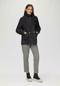 Abrigo marino negro y gris con diseño de doble botonadura, tejido texturizado, bolsillos laterales y una capa acolchada de cuello alto debajo. Complementado con pantalones grises y zapatillas negras.