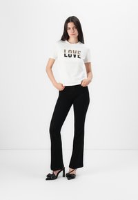 White cotton t-shirt with "LOVE" graphic, paired with fitted black flared pants and black high-heeled shoes. Simple background.