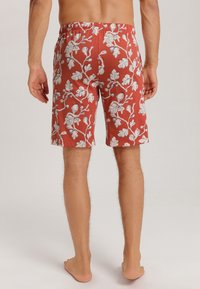 Rote Shorts mit einem weißen Blumen- und Blättermuster, elastischem Bund, knielangem Schnitt und leichtem Stoff. Keine sichtbaren Taschen.