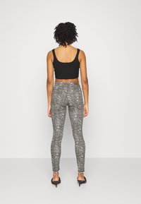 Top corto negro combinado con leggings ajustados de estampado de serpiente en gris y tacones stilettos. Presenta un patrón texturizado en los leggings.