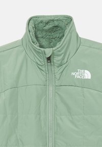 Ljusgrön pufferjacka med hög krage, dragkedjestängning och mjuk inredning. Har North Face-logotypen på bröstet.