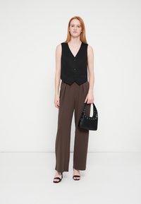 Črna brezrokavnik z tremi gumbi, rjave hlače z visokim pasom, črna torbica za ramo z metalnimi poudarki ter črni sandali z naramnicami.