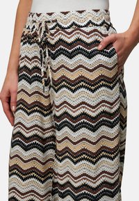 Patterned trousers featuring a zigzag design in black, brown, beige, and white. Includes a drawstring waist and side pockets.