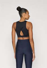 Μαύρο αθλητικό σουτιέν με σχεδιασμό στην πλάτη με άνοιγμα σε σχήμα κλειδιού· συνδυασμένο με ψηλόμεσα κολάν σε ναυτικό μπλε. Ομαλή υφή, εφαρμοστό στυλ, ελάχιστο ορατό λογότυπο.