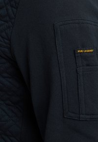 Dunkelblaues Sweatshirt mit gestepptem Muster an den Schultern, ausgestattet mit einer Tasche am Arm und "PME LEGEND"-Branding in Orange.