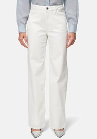 Pantalons larges blancs en denim de coton avec une fermeture éclair et un bouton. Le tissu est lisse avec un léger éclat, adapté à une tenue décontractée.